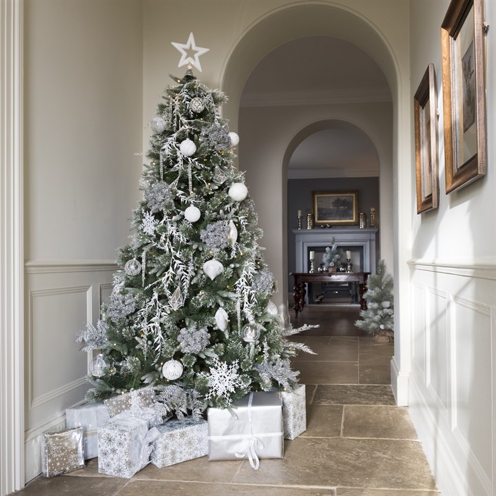 frosted christmas tree with white decorations and christmas presents in a hallway