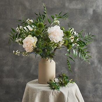 green and white faux floral arrangement in front of grey background