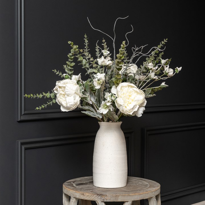 white artificial flowers and foliage stems in a white vases on a small table