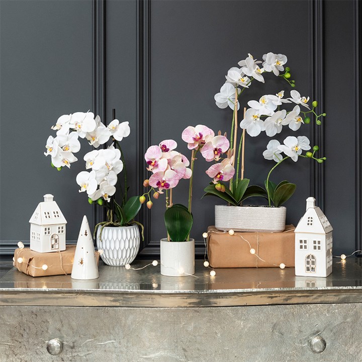 artificial potted orchids and small white ceramic LED house decorations on dresser 