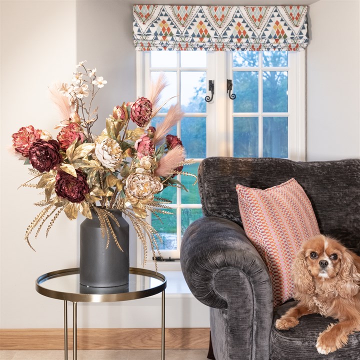 metallic stems and artificial flowers in a churn vase in a living room with dog on sofa