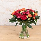 yellow, orange and red artificial ranunculus stems in glass vase