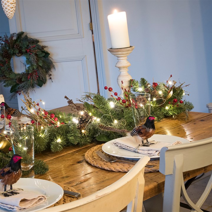christmas table garland with lights, candles and decorative birds on dining table