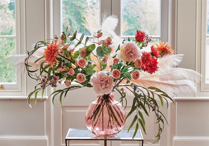 pink, red and orange faux peonies and dahlias arranged with eucalyptus in pink glass vase