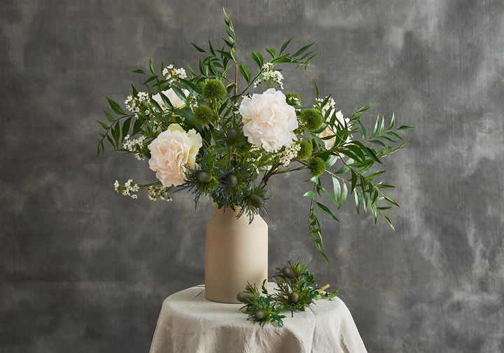 artificial ferns, thistles and white peonies arranged in a white vase