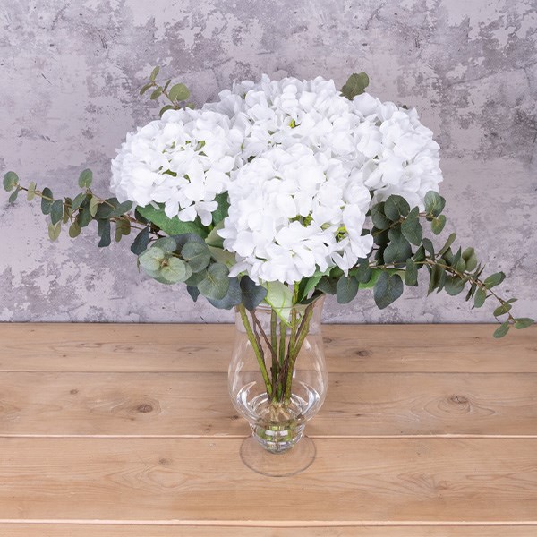 white flowers and eucalyptus arrangement in clear glass vase on a table