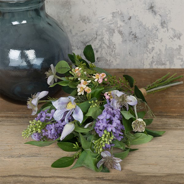 purple and green faux flower bouquet tied with twine on table beside a blue glass vase