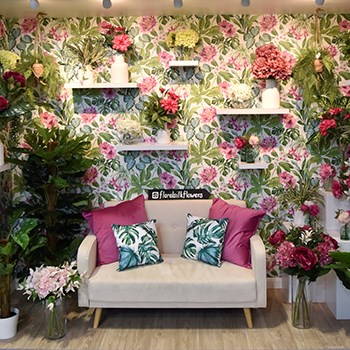 artificial flowers and plants with sofa in front of floral wallpaper