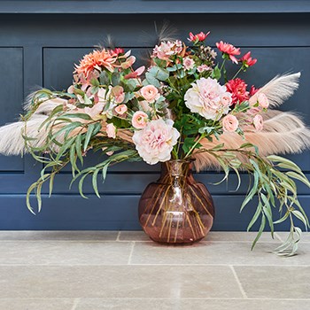 artificial flowers and pampas arranged in a recycled glass vase