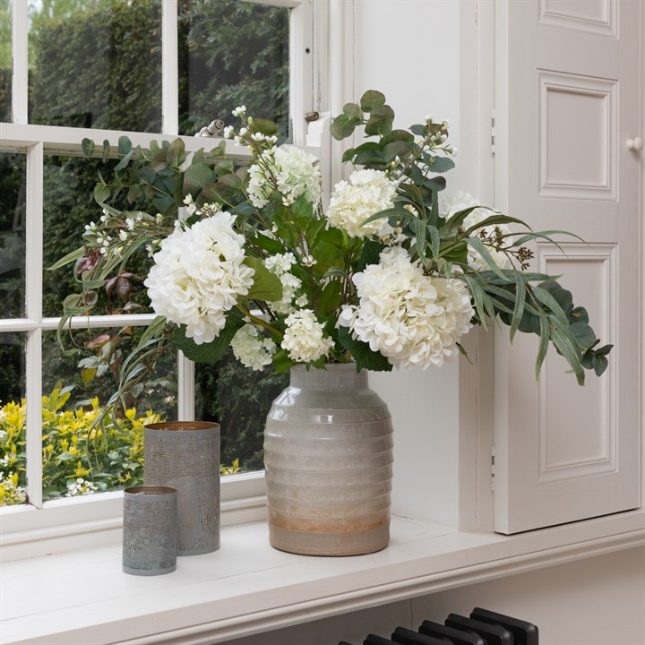 A large bouquet in a vase, white hydrangeas amongst green foliage featuring eucalyptus