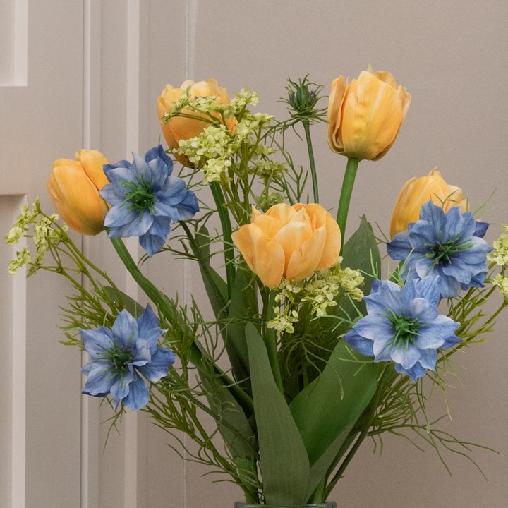 A close up image of a small faux flower bouquet of yellow tulips and blue nigella
