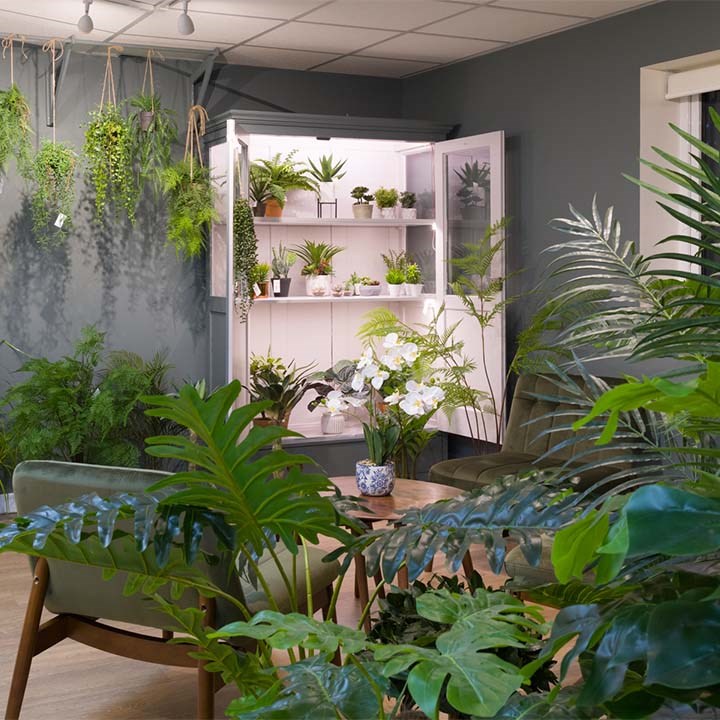 artificial greenery in front of cupboard filled with faux green plants