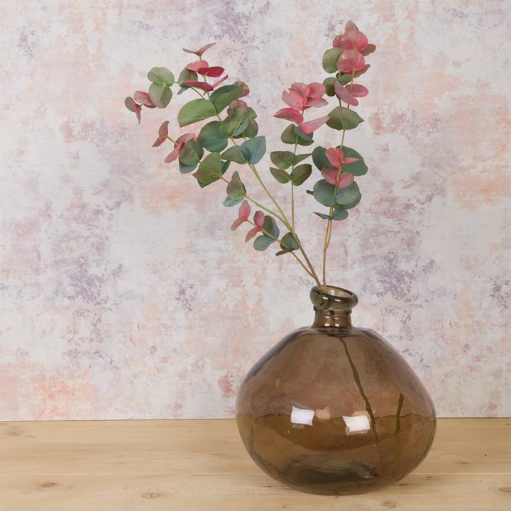 A single stem spray of eucalyptus in a recycled orb vase. The leaves are green and blush pink