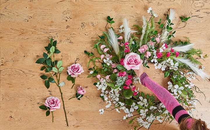 woman's hand inserting a large stem into floral wreath