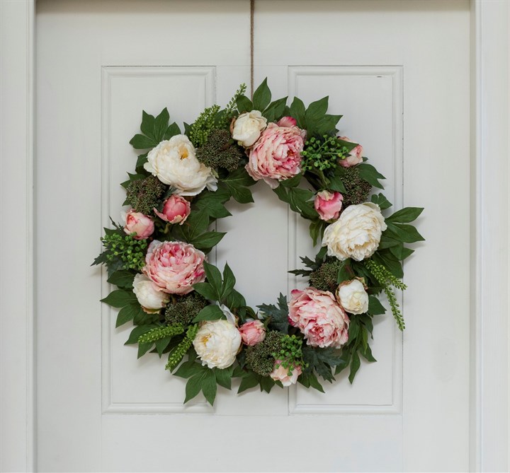 A green wreath on a door with pink and white peonies