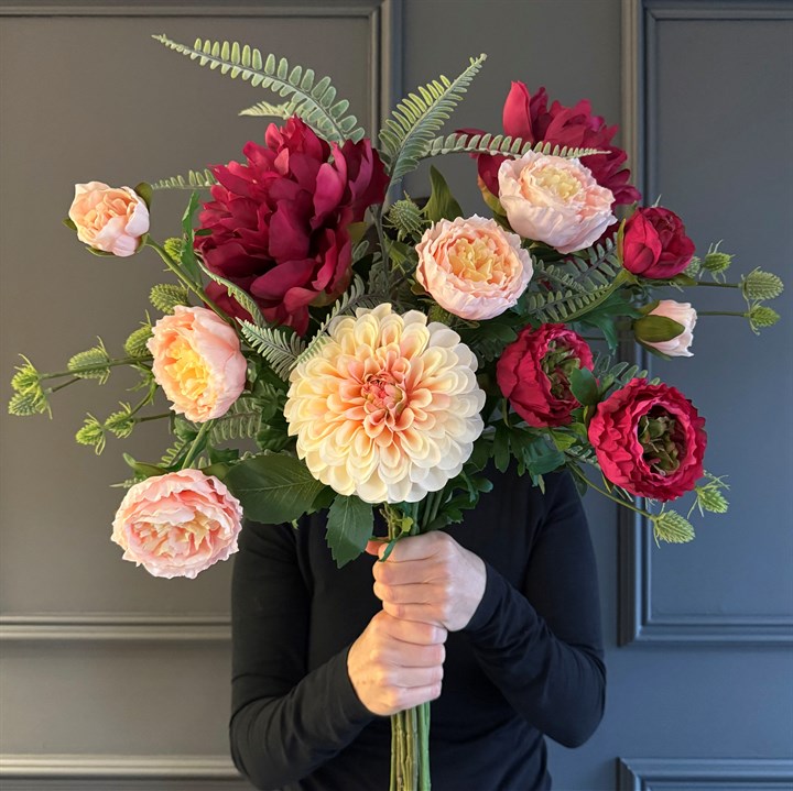 A large beautiful bouquet of realistic looking faux flowers, with peach dahlias and pretty peonies, held in front of someone