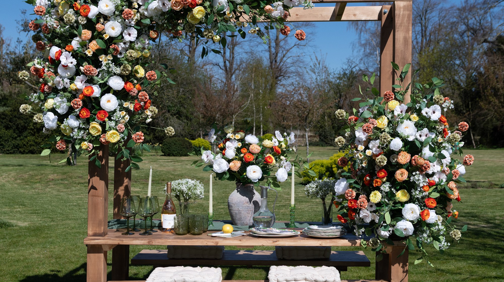 A bouquet of summer flowers in a vase on an outdoor table, with large blooms across the structure