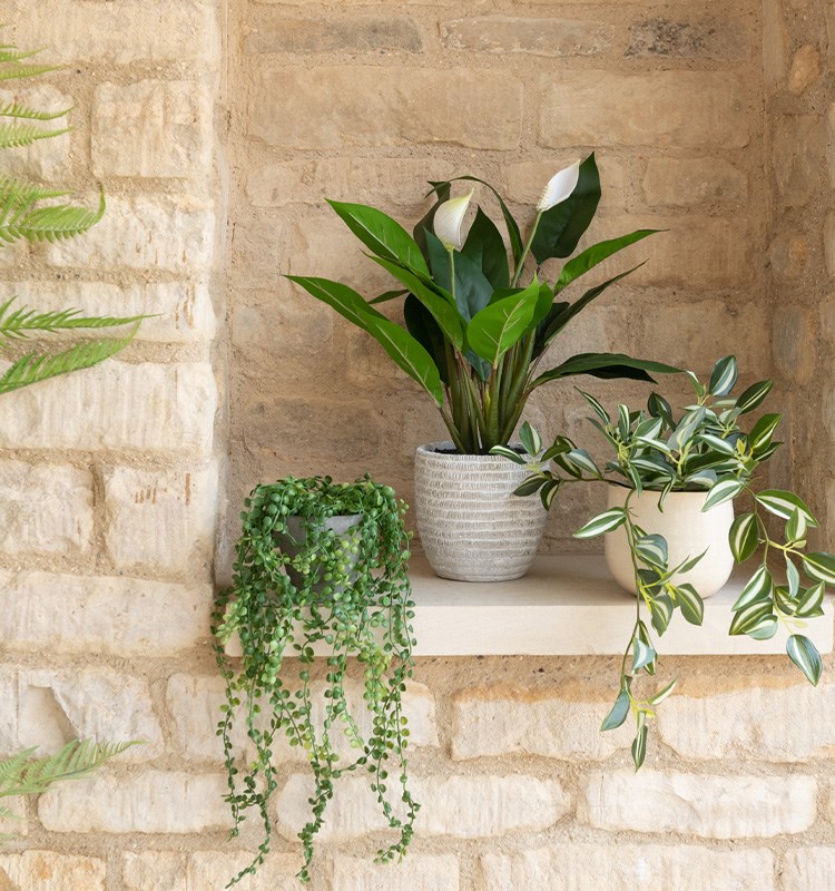 Three beautiful potted faux plants on a brick background