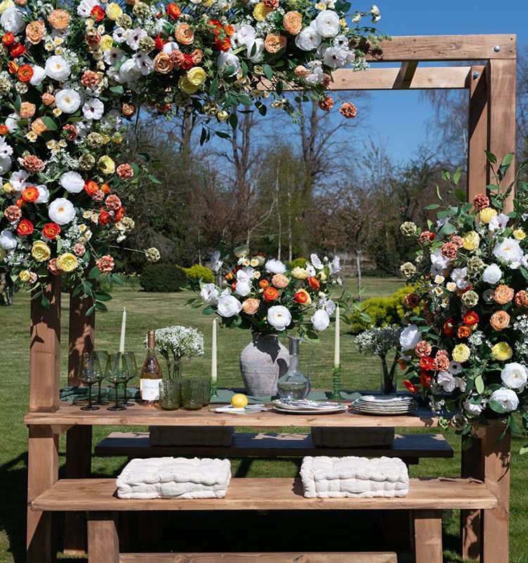 A bouquet of summer flowers in a vase on an outdoor table, with large blooms across the structure