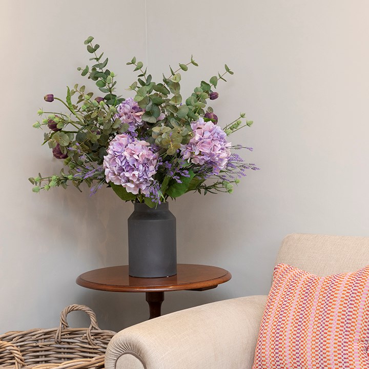 purple faux flowers and artificial eucalyptus arrangement in black vase