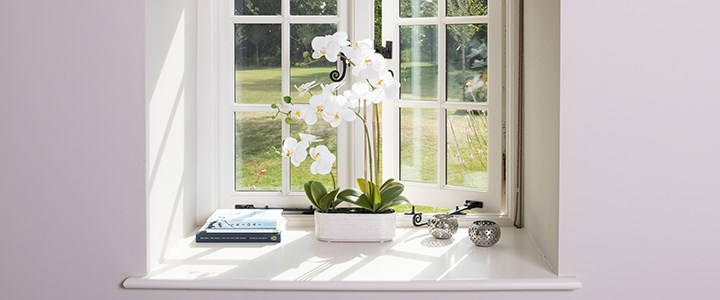 white artificial orchid in long pot on windowsill