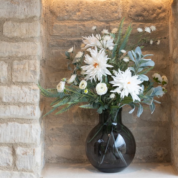 white faux dahlias and foliage arranged in glass vase