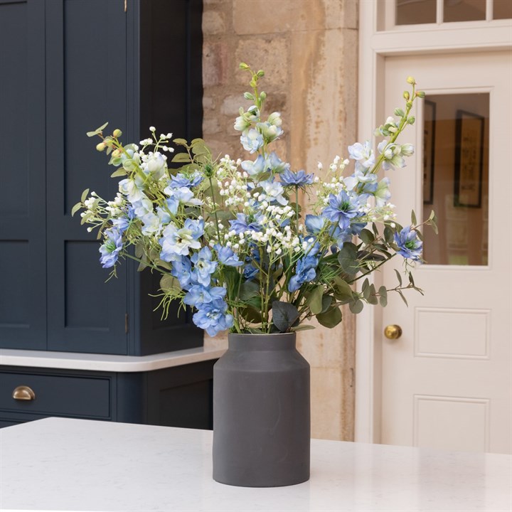 light blue flower arrangement in black churn vase