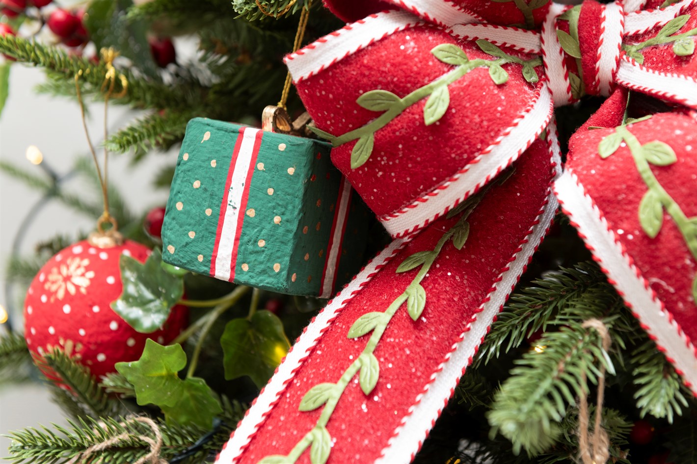 A present decoration hangs on a Christmas tree behind a large christmas bow